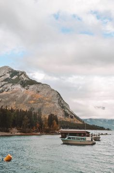 two boats floating on top of a large body of water next to a forest covered mountain