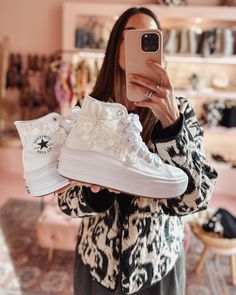 a woman taking a selfie with her cell phone while holding two pairs of sneakers