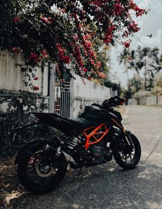 a black and orange motorcycle parked in front of a tree with red flowers on it