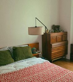 a bedroom with a bed, dresser and lamp on the side table in front of it