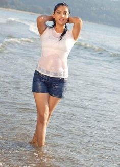 a woman walking in the water with her hand on her head while wearing shorts and a tank top