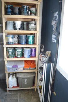 the shelves are filled with paint and buckets on top of each other in front of a refrigerator