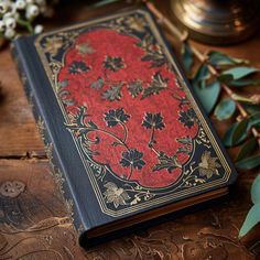 a red and black book sitting on top of a wooden table next to some flowers