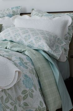 an unmade bed with green and white comforter on it's side, next to a night stand