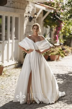 a woman in a white dress standing on a cobblestone street with her arms behind her back