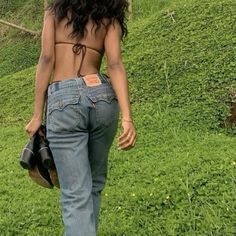 a woman in jeans is walking on the grass with her back turned to the camera