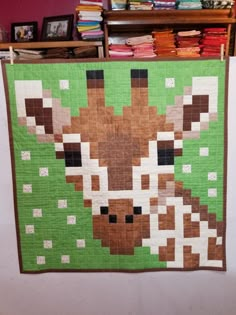 a quilted giraffe is hanging on the wall in front of a bookshelf