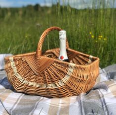 a wicker picnic basket with a bottle of wine in it on a plaid blanket