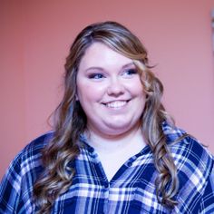 a woman with long hair wearing a blue and white plaid shirt smiles at the camera