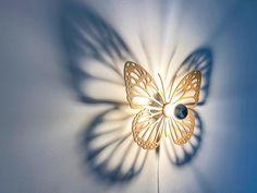 a wall light with a butterfly shaped shadow on it's face and the light shining through its wings