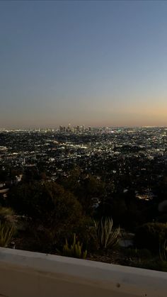 the city lights shine brightly in the distance as seen from atop a hill overlooking an urban area