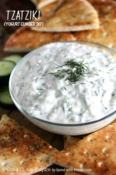 a bowl of tzatzziki dip surrounded by crackers and cucumbers