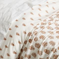 an unmade bed with white sheets and brown floral print on the comforter cover