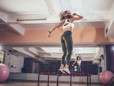 a woman is jumping on a trampoline in a gym