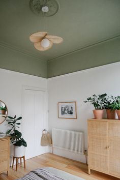 a bedroom with white walls and wooden floors has plants on the dressers next to it