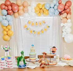 a table topped with cake and balloons in front of a window filled with decorations on top of it