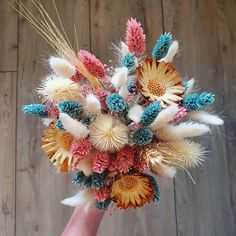 a hand holding a bouquet of flowers on top of a wooden floor