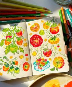 an open notebook with tomatoes on it next to some colored pencils and other art supplies