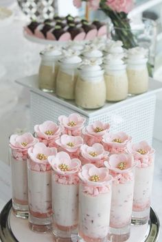 there are many desserts on the table with flowers in vases and jars behind them