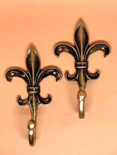 two metal fleur de lis hooks on a pink wall next to each other