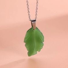 a green leaf shaped pendant hangs from a silver ball chain on a pink background,