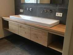 a bathroom sink sitting under a mirror next to a wooden cabinet and counter with two faucets