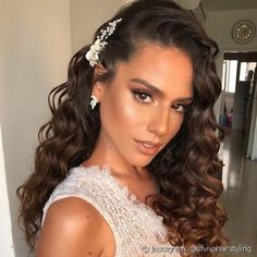 a woman with curly hair wearing a white dress and flower in her hair is looking at the camera