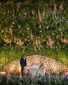 a bride and groom standing in front of a lush green wall with flowers on it