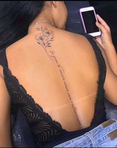 a woman with a flower tattoo on her back is holding a cell phone and looking at the camera