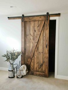 an open barn door in the corner of a room with a vase and flowers on the floor