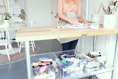 a woman standing at a table with lots of crafting supplies on top of it