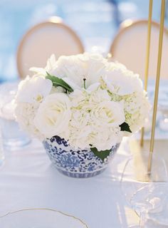 white flowers are in a blue and white vase on a table with gold place settings