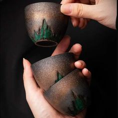 two hands holding small cups with trees painted on them