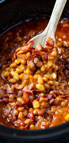 a wooden spoon in a slow cooker filled with beans and meats that is being stirred