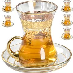 a glass tea cup and saucer with gold trimmings on a plate surrounded by glasses