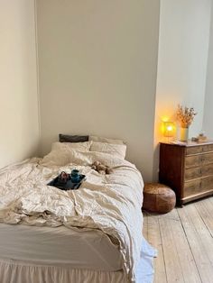 an unmade bed in a bedroom with white walls and wooden flooring next to a night stand