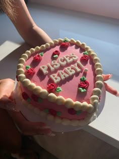 a person holding a pink cake with roses on it and the words peace baby spelled in white frosting