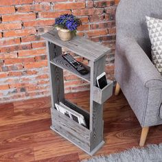 a grey chair sitting in front of a brick wall next to a wooden shelf with magazines on it