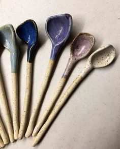 five different colored spoons lined up in a row on a white counter top with speckled paint