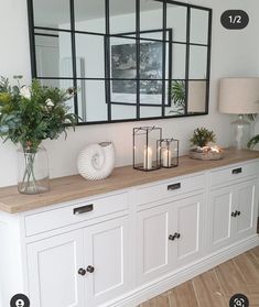 a white buffet with candles and flowers on it in front of a large mirror above the buffet