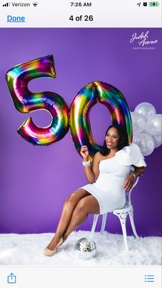 a woman sitting in a chair with balloons and the number 50 on her chest, posing for a photo