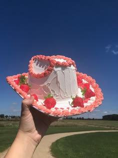 a hand holding up a cake with strawberries on it in front of a blue sky