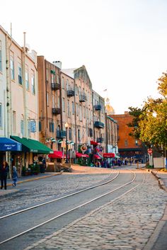 people are walking on the cobblestone street in front of buildings with shops and stores