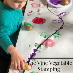 a young boy is painting vegetables on a sheet of white paper with the words, the vine vegetable stamping