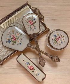 four pieces of antique china with flowers on them sitting on a wooden table next to a comb and spoon