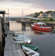 several small boats are docked in the water near a dock with houses and a bridge