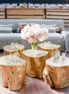 three wooden tables with vases and flowers on them in front of the couches