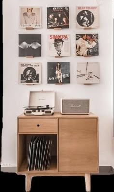 a record player sitting on top of a wooden cabinet in front of a wall covered with records