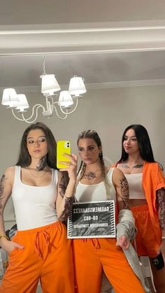 three women in orange pants are holding up a cell phone