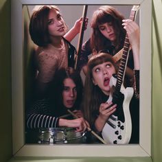 a group of young women standing next to each other in front of a wall with guitars